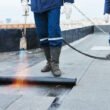 Flat roof installation. Heating and melting bitumen roofing felt by flame torch at construction site